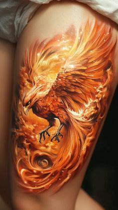 a woman's thigh with an orange and yellow tattoo design on her leg, which has a large bird flying over it