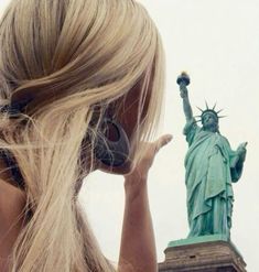 a woman with headphones is looking at the statue of liberty in new york city