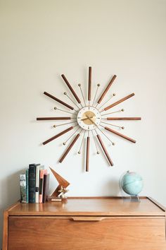 a clock mounted to the side of a wall next to a dresser with books on it