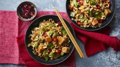 two bowls filled with noodles and vegetables next to chopsticks on a red towel