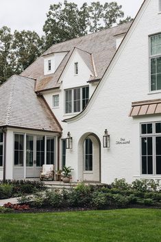 a large white house with lots of windows and plants in the front yard, on a cloudy day