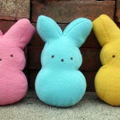 three different colored stuffed animals sitting next to each other on the ground in front of a brick wall