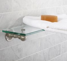 a towel and soap on a glass shelf in a white tiled bathroom with marble tiles