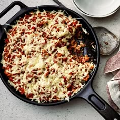 a skillet filled with cheese and sauce on top of a table next to a cup