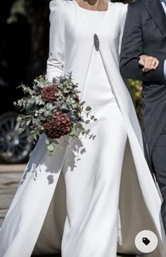 the bride and groom are walking down the aisle together, dressed in white with a pink flower