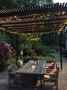 an outdoor dining area with lights strung over the table and bench, surrounded by flowers