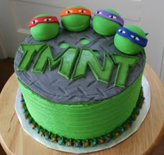 a teenage mutant birthday cake with three ninja turtles on top and the word tmnt spelled out in green frosting