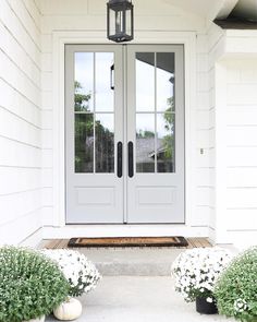 the front door is white and has two pots with flowers in them next to it