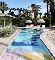 an empty swimming pool surrounded by palm trees and lawn chairs with umbrellas in the background