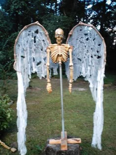 a skeleton with angel wings is standing in the grass next to a tree stump and some branches