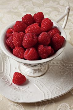 a white bowl filled with raspberries sitting on top of a lace doily