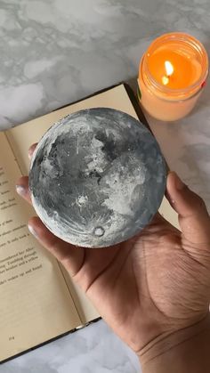 a person holding up a small metal plate next to an open book with a candle on it