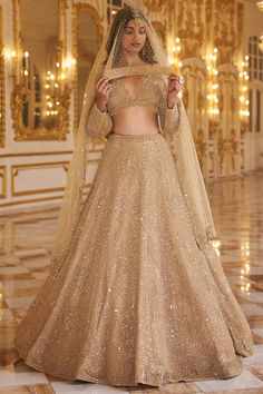 a woman in a gold gown and veil standing on a marble floor with chandelier