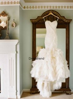 a wedding dress hanging on a mirror in front of a wall with a wooden frame