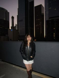 a woman standing on top of a roof in front of some tall buildings at night