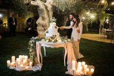 a newly married couple cutting their wedding cake in front of lit candles on the lawn