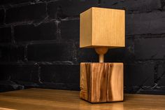 a wooden table with a lamp on top of it in front of a brick wall