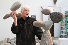 an older man juggling rocks on top of each other in front of a rock sculpture