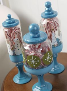 three glass jars filled with candy canes on top of a wooden table