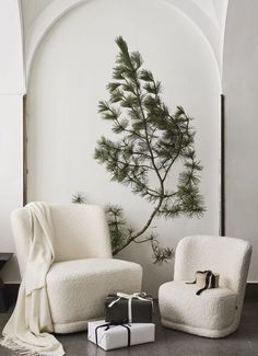 two white chairs sitting next to each other in front of a wall with a tree on it