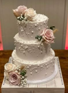 a three tiered white wedding cake with pink and white flowers on the top layer