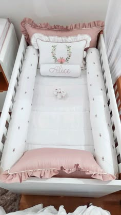 a baby crib with pink and white bedding, pillows and blankets on it