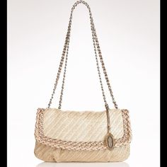 a beige purse with chain handles and an oval clasp on the front, sitting on a white surface