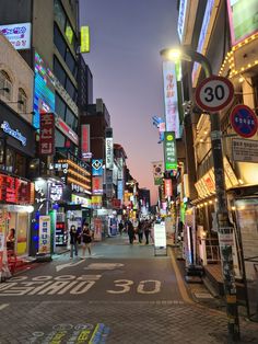 a city street with people walking on the sidewalk and buildings in the background at night