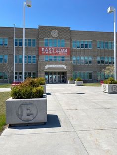 an empty parking lot in front of a large building with flags on the poles and bushes