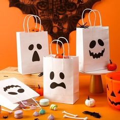 three halloween bags with faces on them and candy in front of an orange wall behind them