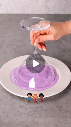 someone is holding a wine glass with purple liquid in it and two small figurines are on the plate