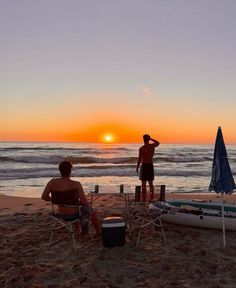 two people sitting on chairs at the beach watching the sun set