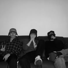 three people sitting on a couch with their hands covering their faces while one person covers his mouth