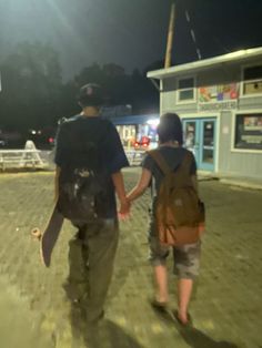 two people holding hands while walking down the street at night with their skateboards in hand