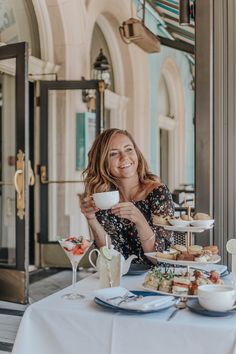 a woman sitting at a table with food and drinks in front of her, smiling