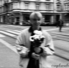 a man holding flowers in his hands while walking down the street with buildings behind him