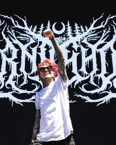 a man in white shirt and black pants with tattoos on his arm holding up a red frisbee