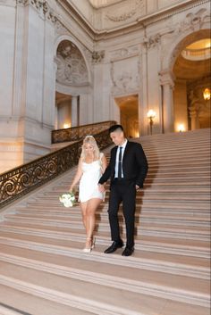 a bride and groom are walking down the stairs in an elegant building with chandeliers