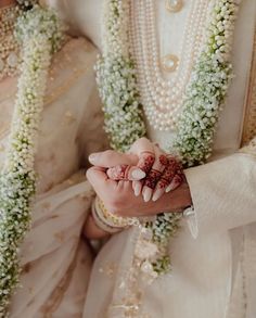 a man and woman dressed in white holding hands with flowers all around their necks