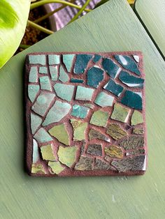 a green table with a small mosaic tile on it's surface next to a potted plant