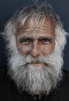 an old man with white hair and blue eyes looks into the camera while wearing a black shirt