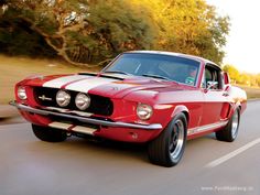 an old red mustang driving down the road