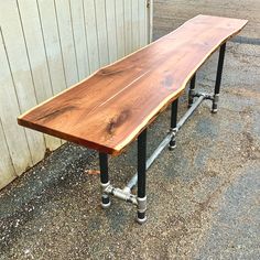 a long wooden table sitting on top of metal pipe legs in front of a building