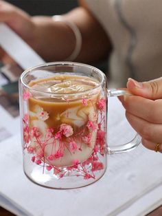 a person is holding a coffee mug with flowers on it and writing in a notebook