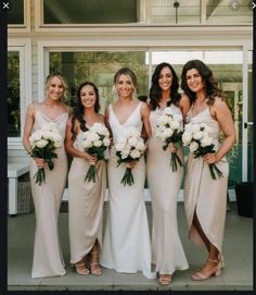 a group of women standing next to each other in front of a building holding bouquets