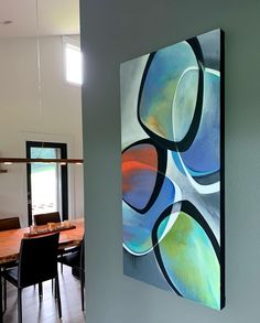 an abstract painting hangs on the wall next to a dining room table and chair set