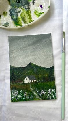 a white plate with a painting on it next to a paintbrush and some other items