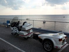 a motorcycle parked next to a car on the side of a road near the ocean