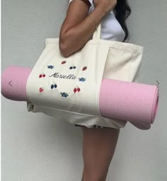 a woman is holding a pink yoga mat and a tote bag with berries on it