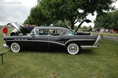 an old black car parked on top of a lush green field